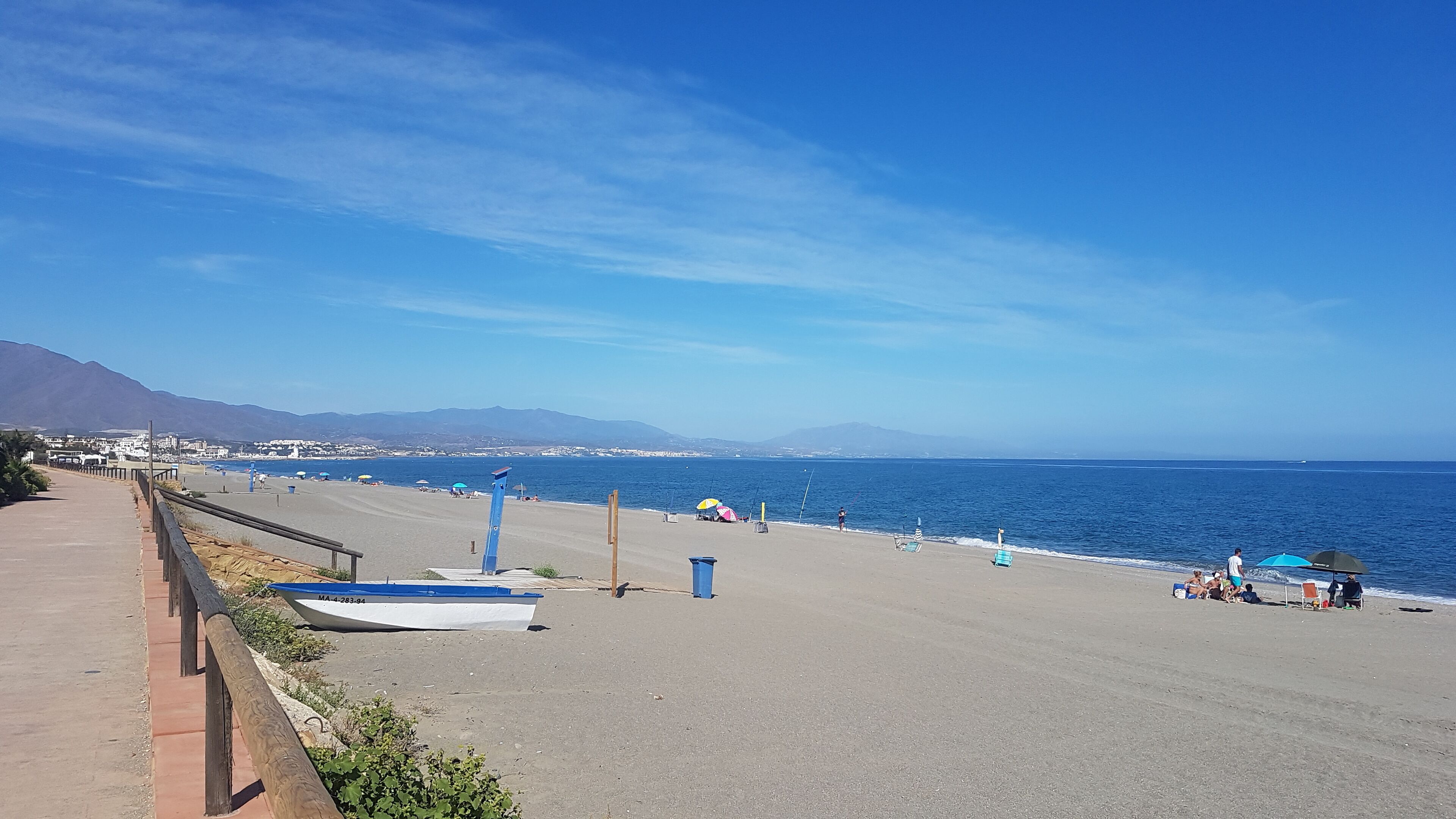 A coastal road with a beach, a parked boat, and a clear view of the sea.