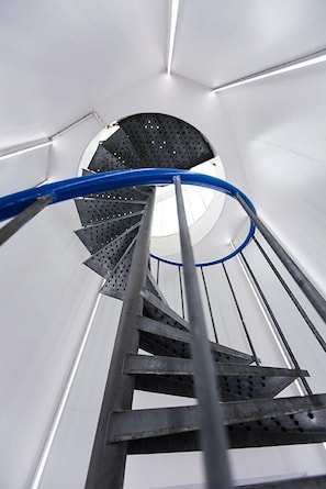 Un escalier en colimaçon en métal, doté d’une main courante bleue, qui mène à une plateforme circulaire.