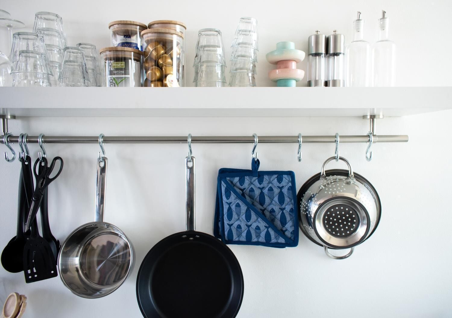 A kitchen with hanging utensils, pots, and jars on a shelf.