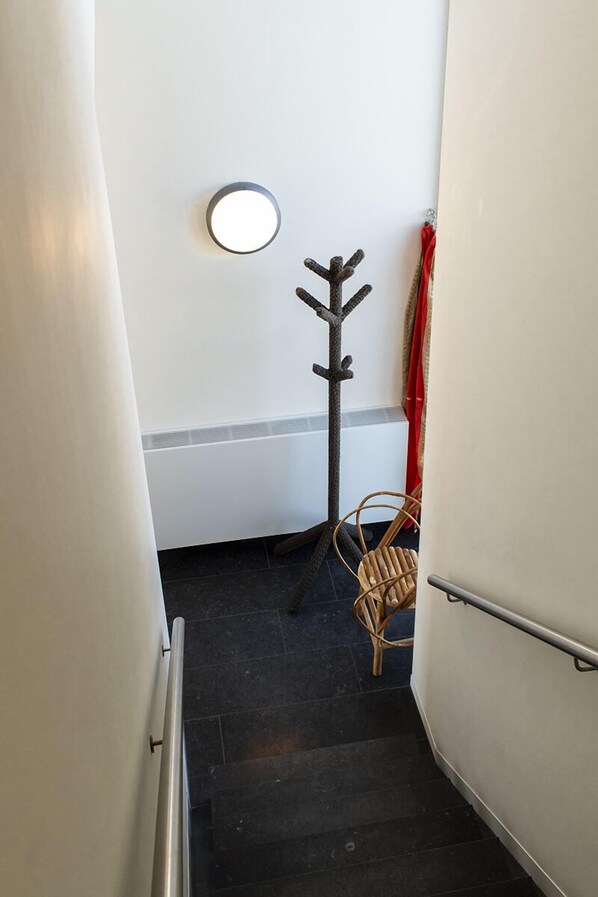 A narrow stairway with a coat rack and a chair, leading to a room with a white wall and a red curtain. - SWEETS - Sluis Haveneiland (Amsterdam)