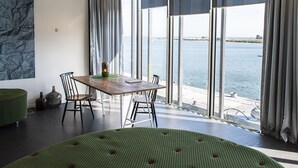 Una habitación moderna con un ventanal grande con vistas a un cuerpo de agua, una mesa de madera con sillas y un sofá verde estampado.