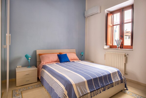 A bedroom with a bed, a nightstand, a lamp, and a window with curtains.