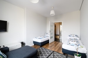 A modern, compact room with two beds, a sofa, a flat-screen TV, and a small table. - Labo Apartment Tamka (Warsaw)