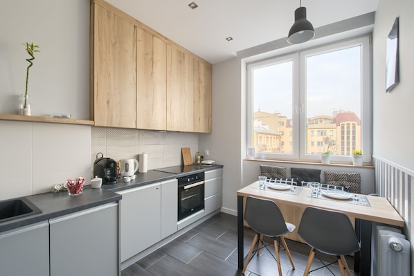 A modern kitchen with a dining area, large windows, and a view of buildings. - Labo Apartment Tamka (Warsaw)