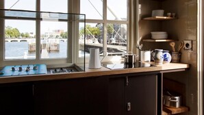 A kitchen with a view of a canal, a stove, and shelves with dishes and utensils. - SWEETS - Amstelschutsluis (Amsterdam)