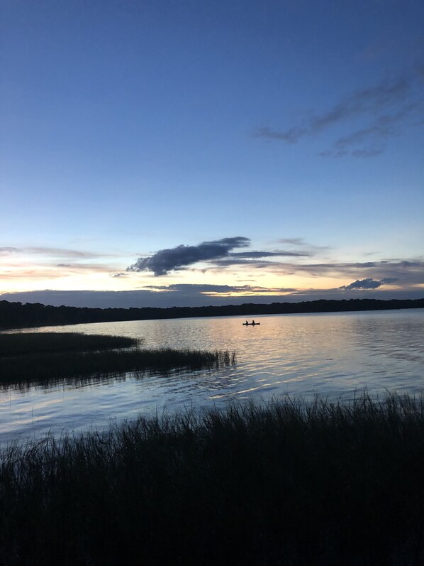 A calm lake with a silhouette of a boat in the distance, surrounded by grassy areas and a clear sky. - LAKESIDE BREEZE on Lake Eustis Harris Chain of Lakes Central Florida (Tavares)