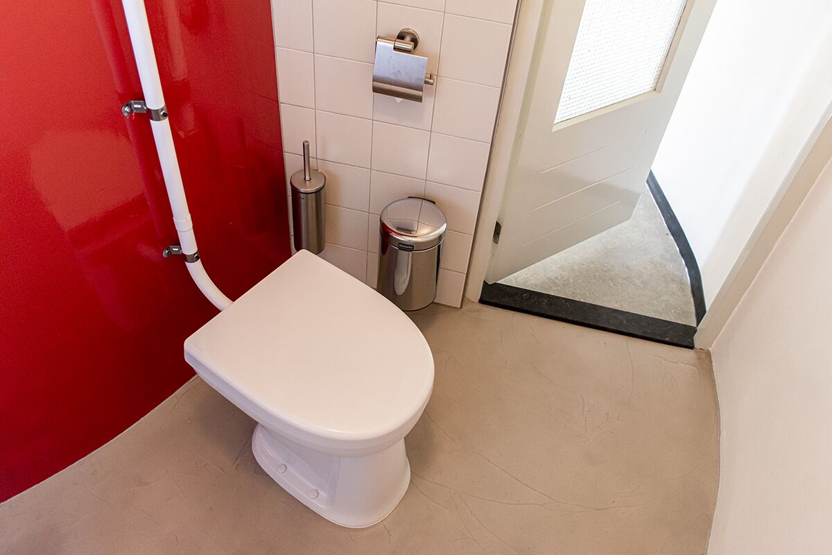Un baño pequeño y moderno con inodoro blanco, pared roja y piso de baldosas blancas.