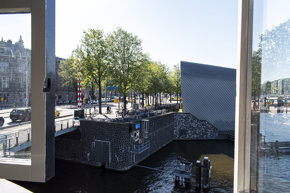 Une vue sur un canal, un pont en pierre, un bâtiment moderne à la façade géométrique et une rue où l’on voit des voitures et des vélos.