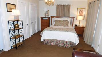 Een slaapkamer met een bed, een houten nachtkastje, een lamp, een kast, een stoel en een kroonluchter.