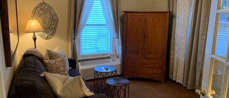 Una sala de estar acogedora con un sofá, una lámpara, una ventana con cortinas, un mueble de madera y una mesita.