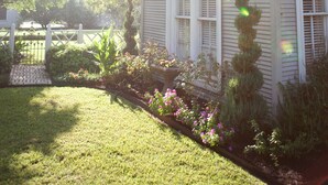 A house with a well-maintained lawn, a small garden with various plants and flowers, and a white fence in the background. - Rainbow Courts Motel (Rockdale)