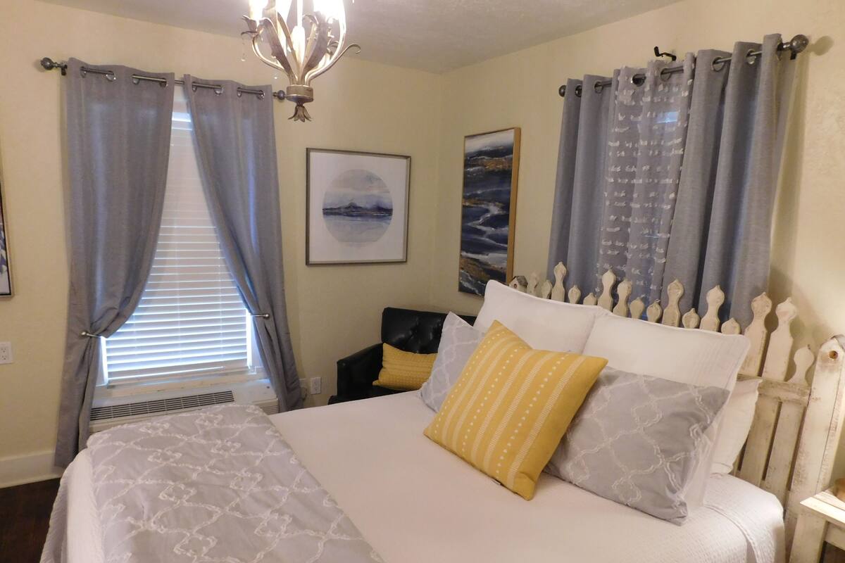 A bedroom with a bed, a nightstand, a chair, and a window with curtains.