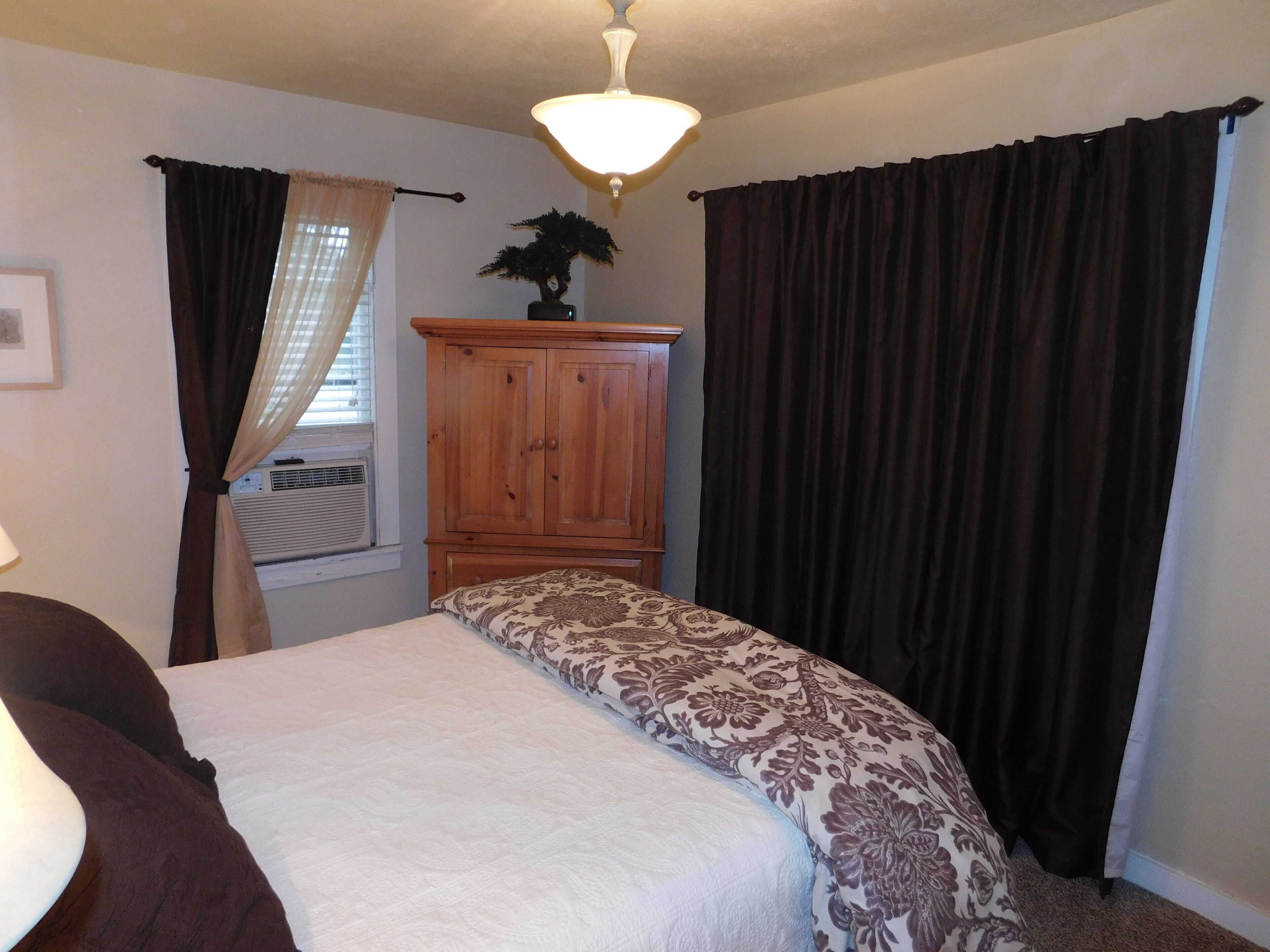 Un dormitorio con cama, armario de madera, ventilador de techo y ventana con cortinas.