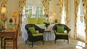 A cozy bedroom with a bed, two wicker chairs with green cushions, a small table, and a vase with flowers. - Rainbow Courts Motel (Rockdale)