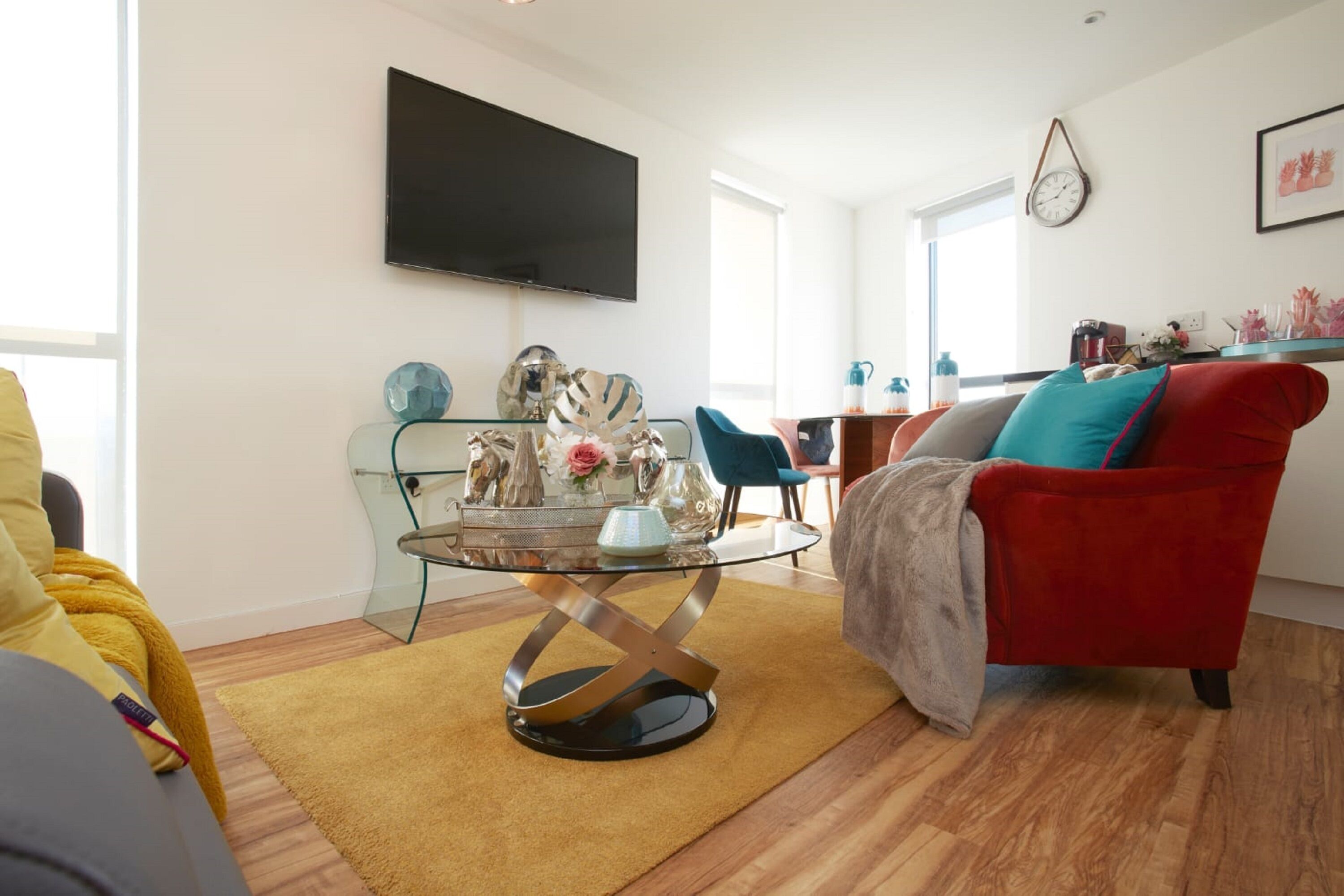 A modern living room with a glass coffee table, a red armchair, and a yellow sofa.