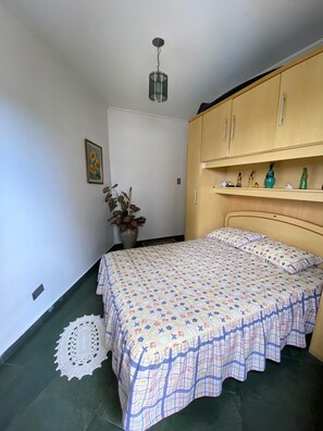 A bedroom with a bed, a wooden wardrobe, a hanging light fixture, a framed picture, and a potted plant. - Apt well decorated and complete 50 meters from the beach + beach service (Vila Clais)