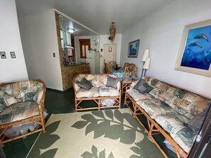 A living room with a sofa set, a dining table with chairs, a kitchen area, and a painting on the wall. - Apt well decorated and complete 50 meters from the beach + beach service (Vila Clais)