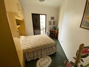 A small, narrow hotel room with a bed, a wooden wardrobe, a small table with a television, and a fan. - Apt well decorated and complete 50 meters from the beach + beach service (Vila Clais)