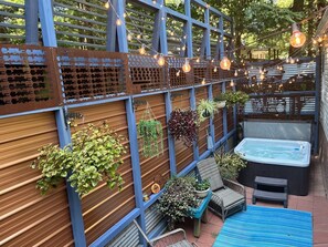 A patio area with a wooden fence, hanging plants, a hot tub, and outdoor seating. - Adventure Launchpad or Cosy Resting Space (Asheville)