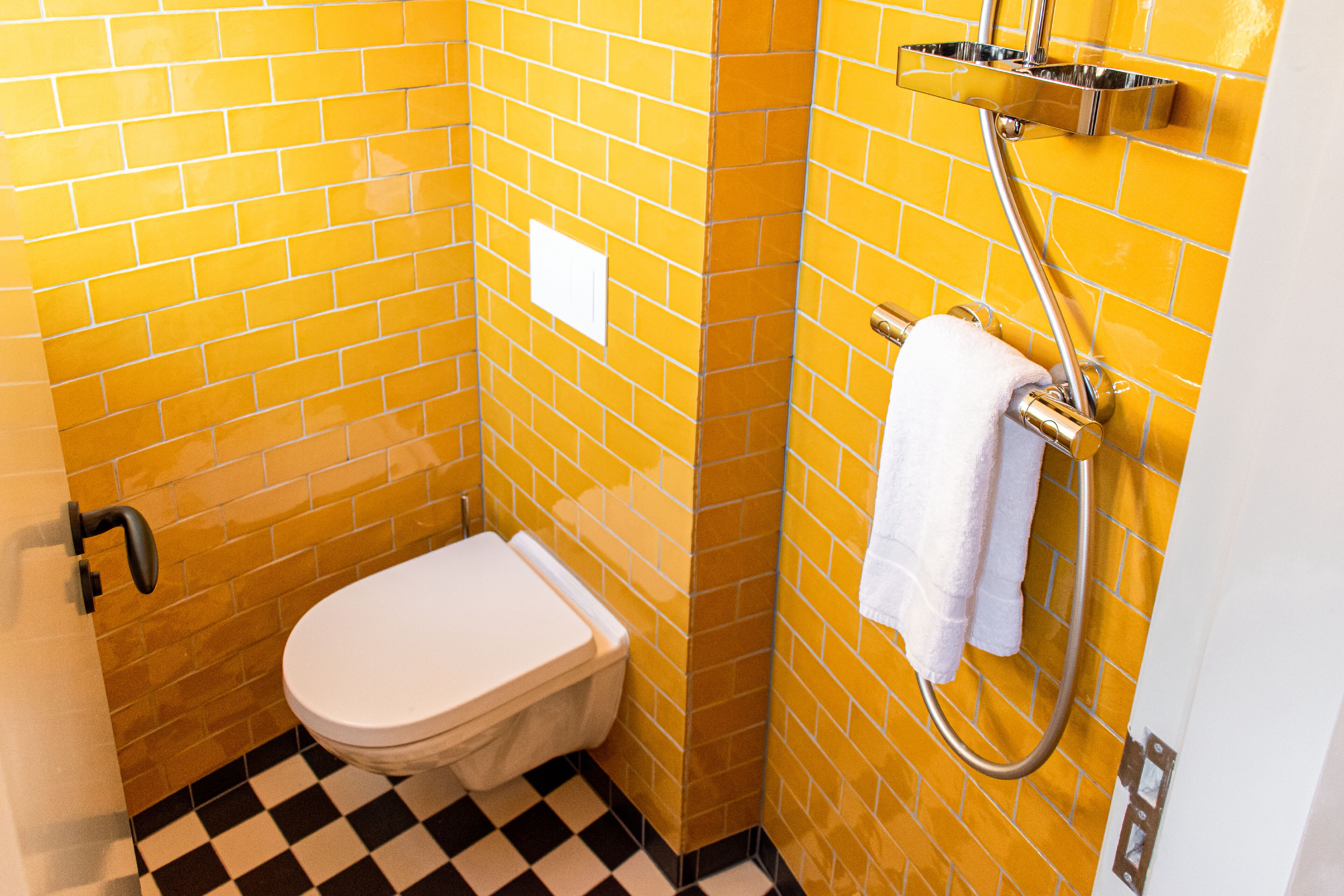 Un baño pequeño con azulejos amarillos, un inodoro blanco y una zona de ducha.