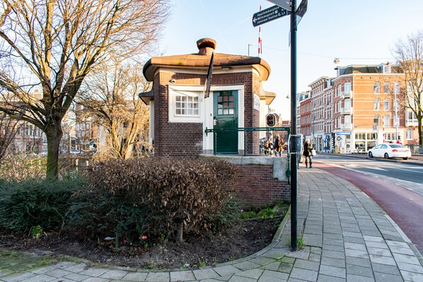 A small brick building with a green door, surrounded by trees and a sidewalk. - SWEETS - Willemsbrug (Amsterdam)
