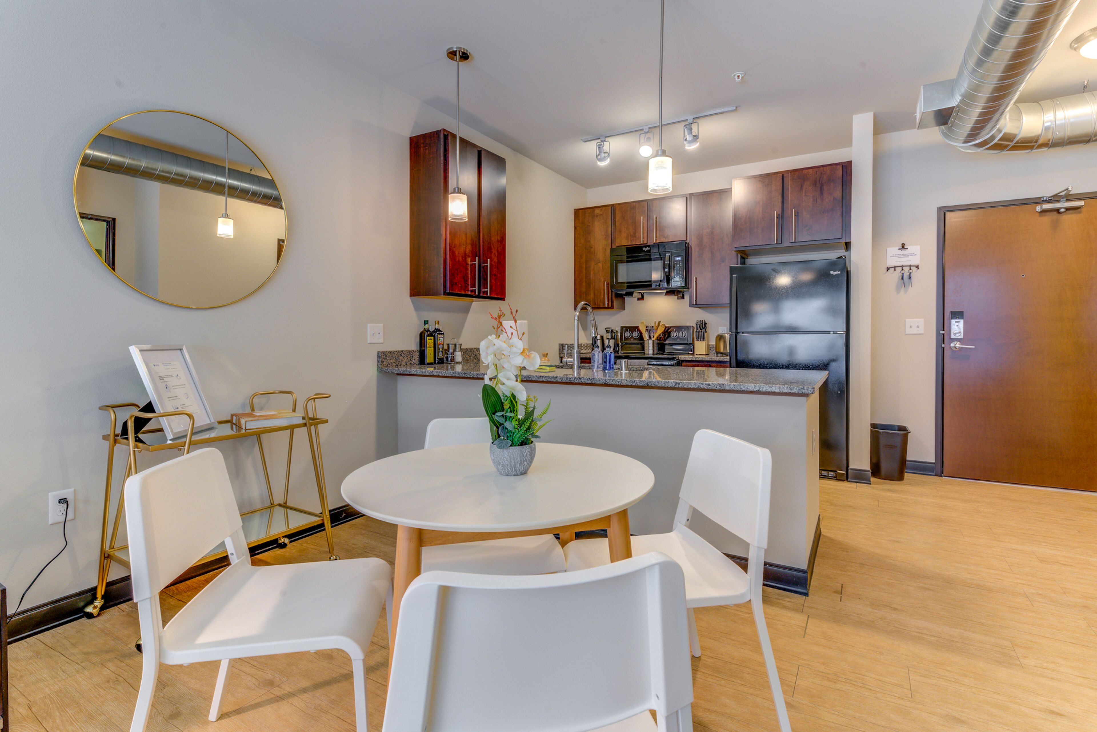 Een moderne keuken met donkerhouten kasten, roestvrijstalen apparatuur en een witte eethoek met een ronde tafel en stoelen.