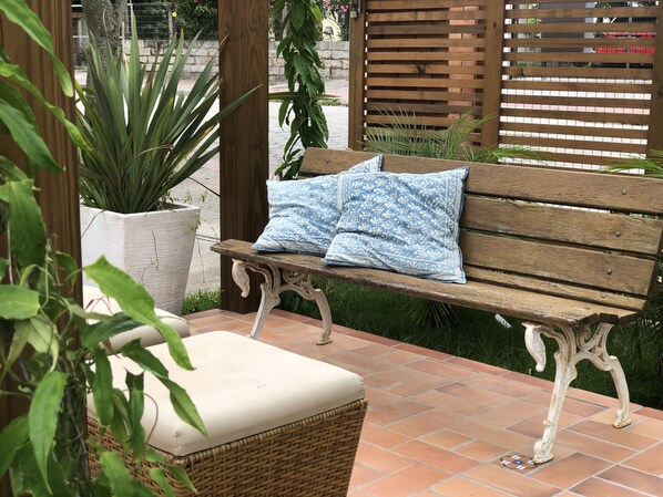A wooden bench with white cushions, a wicker ottoman, and a potted plant. - Pousada Poente do Sol (Garopaba)