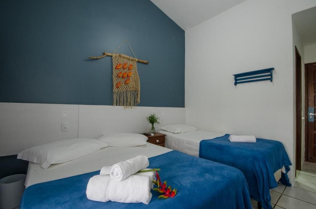 A hotel room with two beds, a blue wall, a macrame wall hanging, and a small plant.