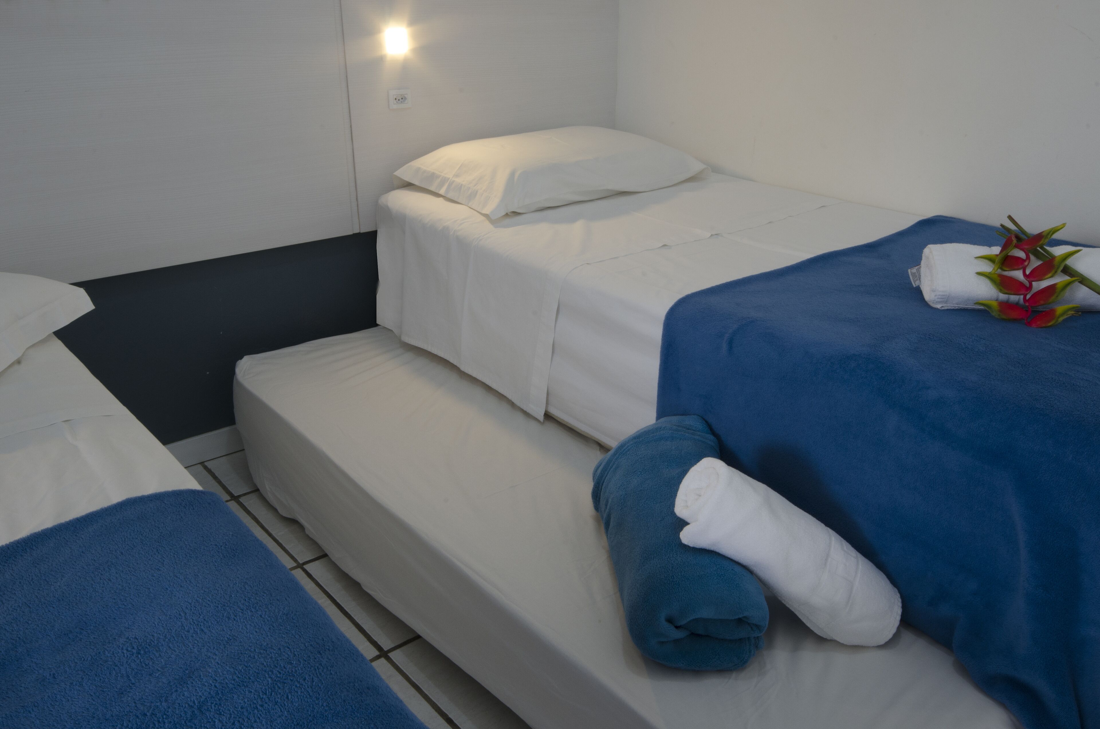Ett hotellrum med två sängar, var och en med ett blått och vitt täcke, ett litet trappsteg mellan dem och en väggmonterad lampa.