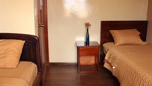 A hotel room with two beds, a nightstand with a vase, and a wooden door. - Hotel Norte (Cuenca)