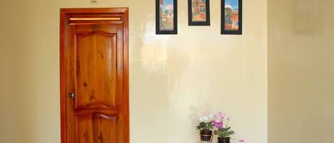 Una puerta de madera, tres cuadros enmarcados en la pared y dos plantas en macetas sobre un soporte metálico.