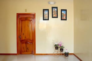 Une porte en bois, trois tableaux encadrés accrochés au mur et deux plantes en pot posées sur un présentoir en métal.