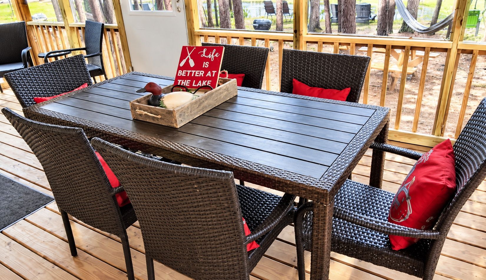 An outdoor dining area with wicker chairs and a wooden table, featuring a sign that reads 'Life is better at the lake.'