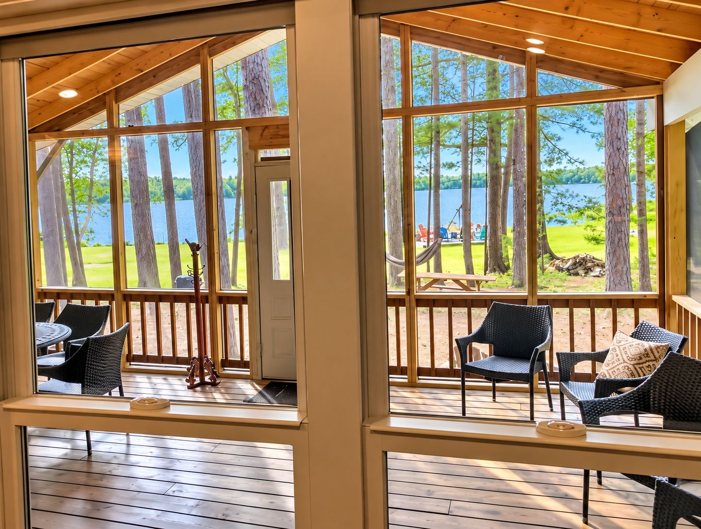 A wooden deck with outdoor seating, large windows overlooking a lake, and a view of the surrounding trees.