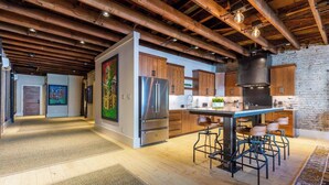 A modern kitchen with wooden cabinets, a stainless steel refrigerator, and a bar area with stools. - Historic Loft in the Heart of Downtown Morganton (Morganton)