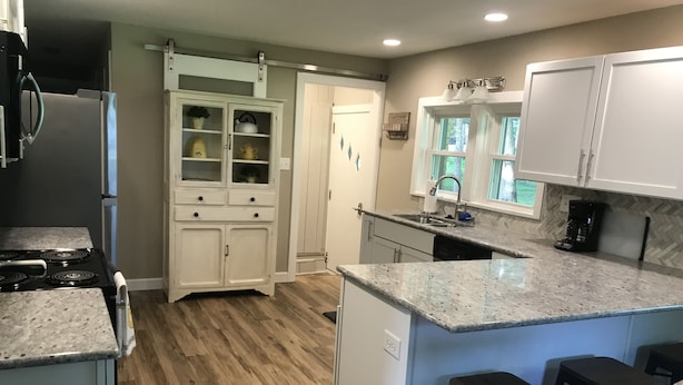 A modern kitchen with a granite countertop, wooden flooring, and white cabinetry. - Nagawicka Woods-Beautiful Lake Country Ranch Home (Delafield)