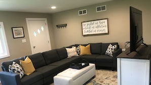 A living room with a sectional sofa, a white ottoman, a flat-screen TV, and a motivational quote on the wall. - Nagawicka Woods-Beautiful Lake Country Ranch Home (Delafield)