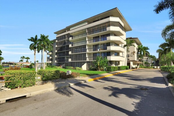 A multi-story hotel with balconies, a parking lot, and palm trees. - Condo in Community With Beach Access, Pool and Tennis (Marco Island)