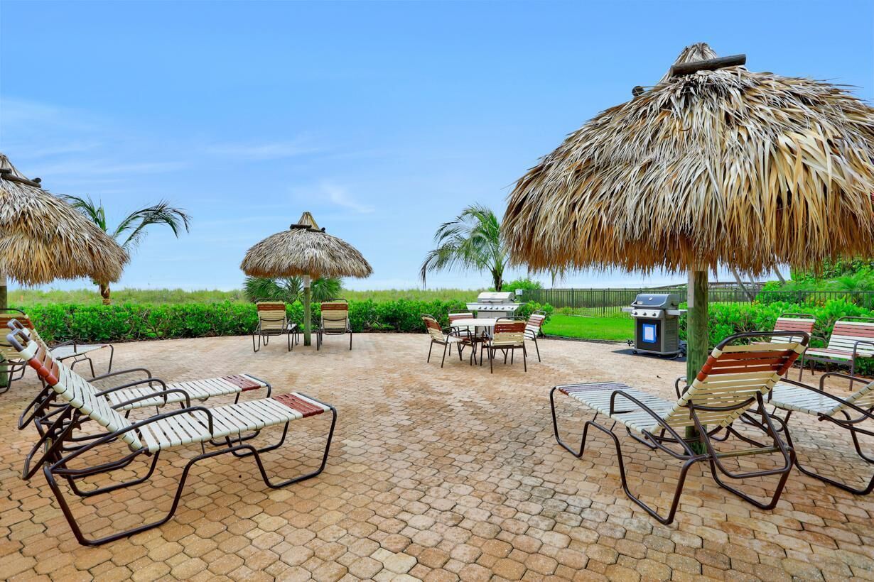 A patio with lounge chairs, a table, and thatched umbrellas.