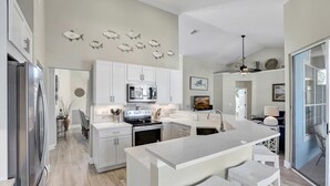 A modern kitchen with white cabinetry, a central island, and a dining area with bar stools. - Lovely Pet-friendly Waterfront Home With Pool and Dock (Marco Island)
