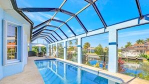A swimming pool with a glass ceiling, surrounded by a poolside area with chairs and umbrellas. - Lovely Pet-friendly Waterfront Home With Pool and Dock (Marco Island)