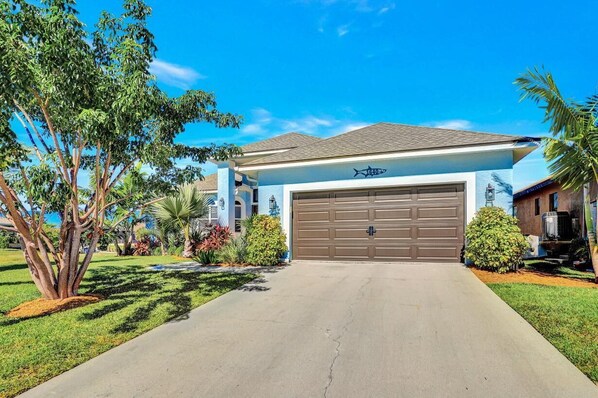 A residential house with a garage, surrounded by well-maintained lawns and trees. - Lovely Pet-friendly Waterfront Home With Pool and Dock (Marco Island)