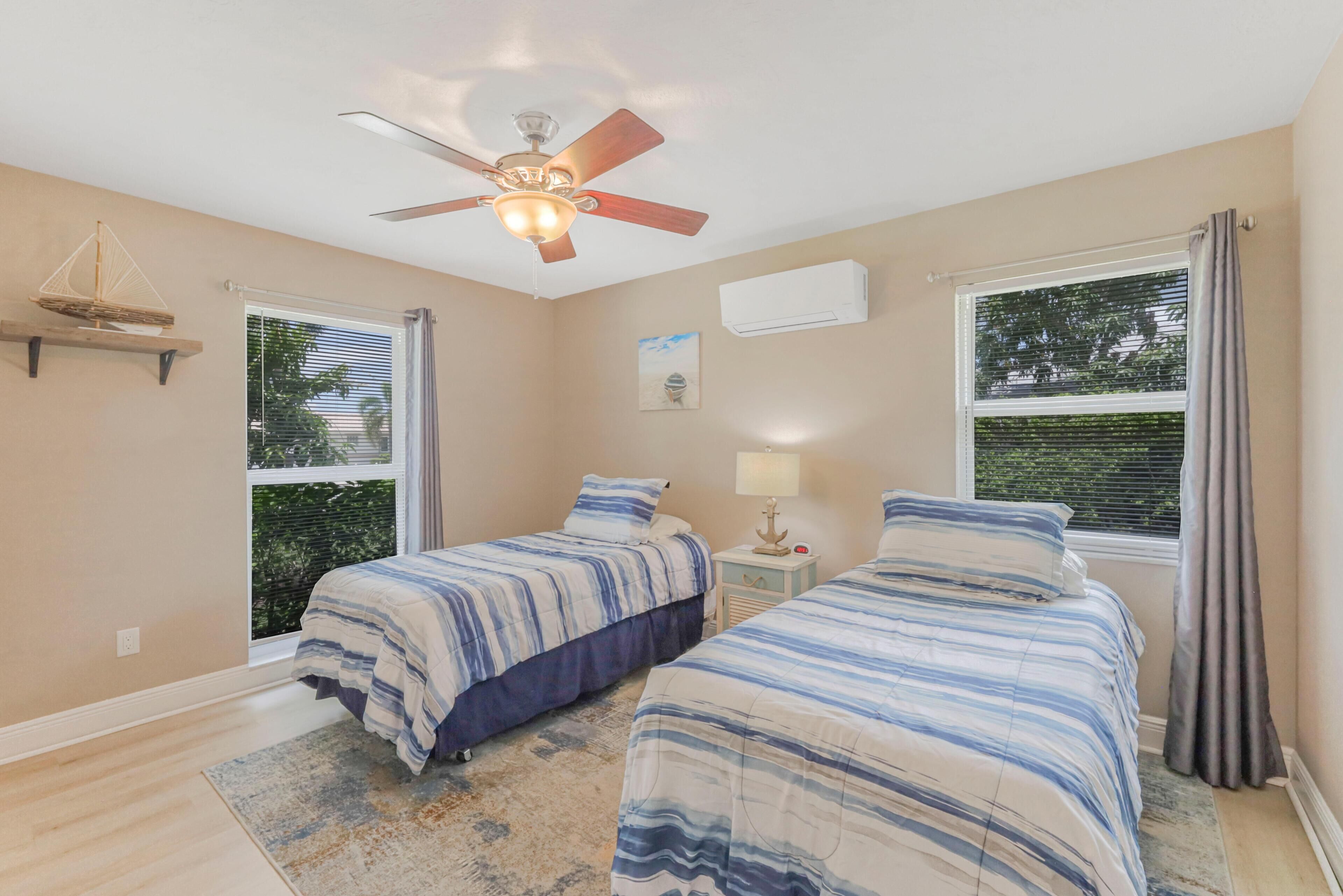 A bedroom with two beds, a ceiling fan, an air conditioning unit, and a window with blinds.