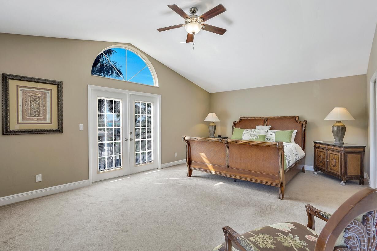 A bedroom with a bed, two bedside tables, a ceiling fan, and a large window.