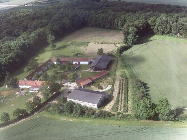 An aerial view of a rural property with multiple buildings, including a large barn and several smaller structures, surrounded by fields and dense forest. - Domaine de collen (Lépine)