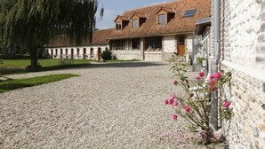 A stone building with a gravel driveway, a wooden fence, and a tree. - Domaine de collen (Lépine)