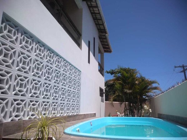 A swimming pool with a geometric wall design, a clear blue sky, and a palm tree.