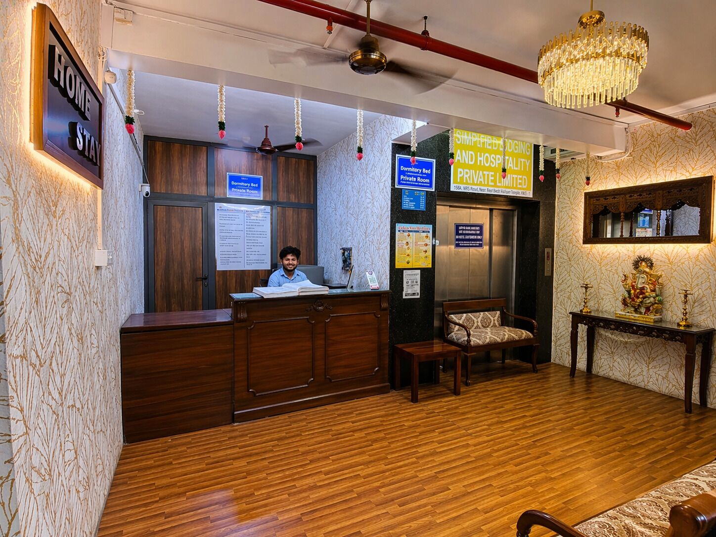 A hotel reception area with a wooden reception desk, a chandelier, and a sign indicating private rooms.