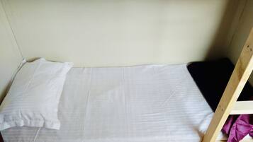 Un lit superposé avec un matelas blanc et un oreiller, une tête de lit en bois portant le numéro 33, et une petite étagère en bois recouverte d’un tissu violet.