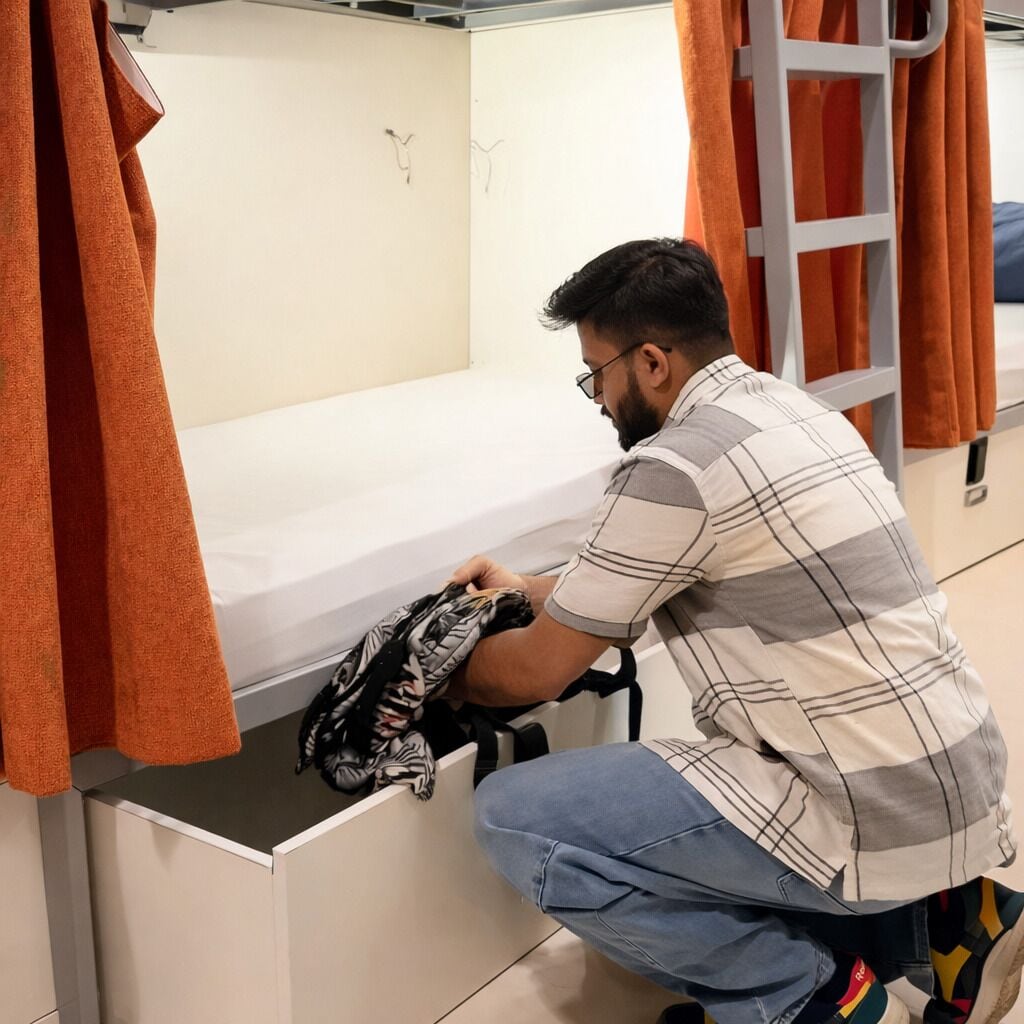 A person organizing clothes in a compartment of a bunk bed.